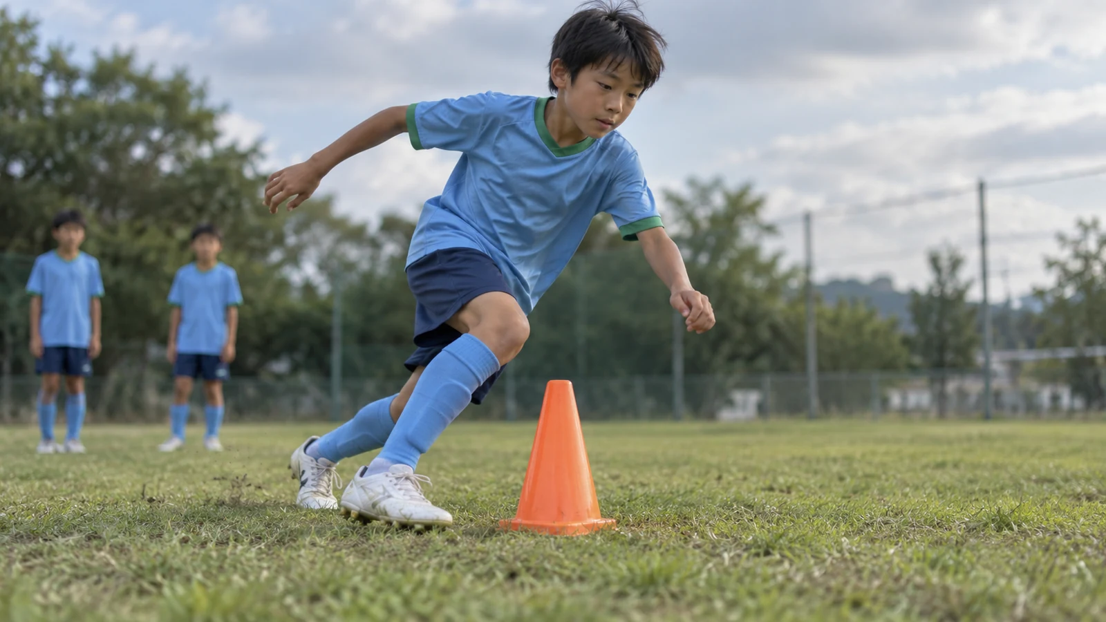 オレンジ色のコーンの横で踏み込み、方向を変える小学生サッカー選手