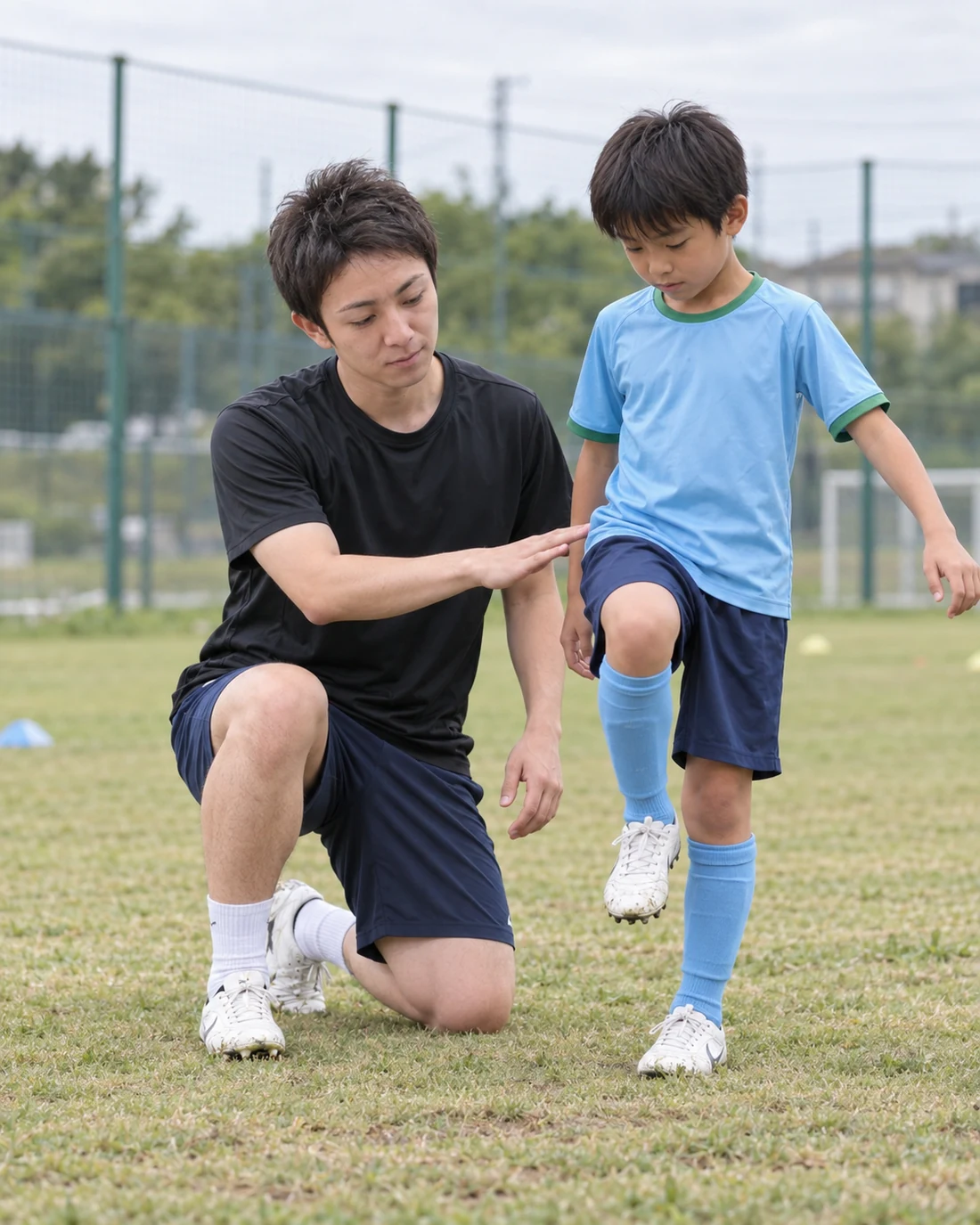 黒いシャツのコーチが小学生選手と目線を合わせて動作を伝える様子
