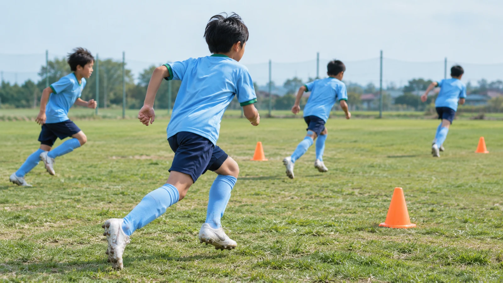 芝生グラウンドでコーンに向かって走り出す小学生サッカー選手