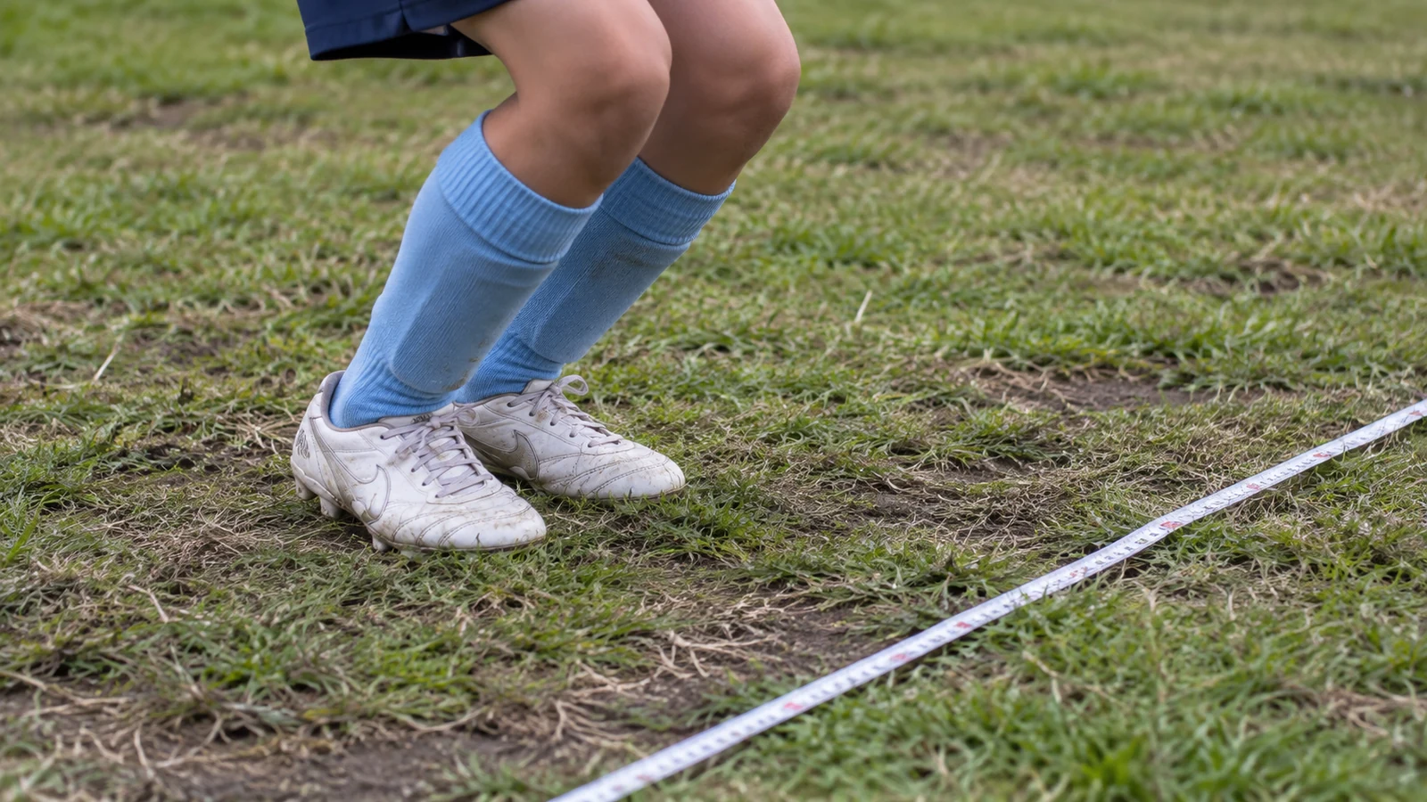 芝生のメジャーを目印に立ち幅跳びを行う小学生選手の足元